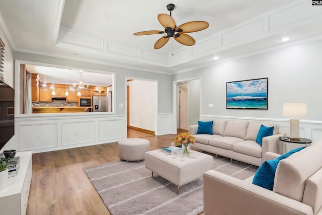 living area featuring wood finished floors, a ceiling fan, a decorative wall, crown molding, and wainscoting