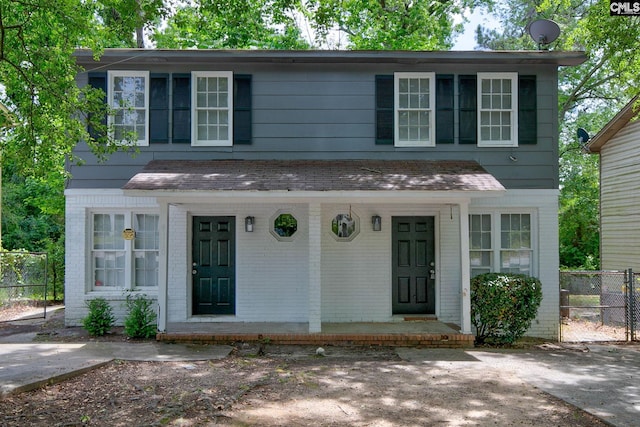 view of front of property with brick siding, covered porch, fence, and roof with shingles