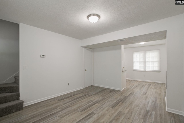 basement with light wood-style flooring, stairway, a textured ceiling, and baseboards