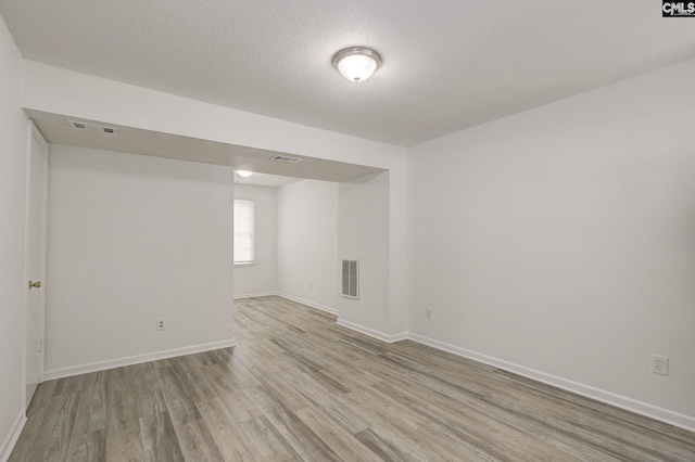 below grade area featuring light wood-style floors, baseboards, and a textured ceiling