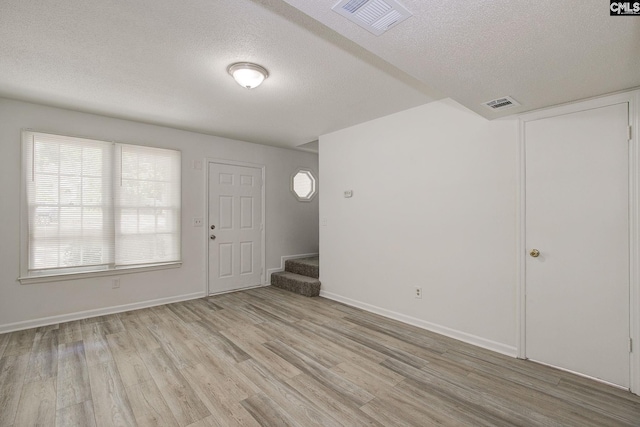 entrance foyer with a textured ceiling, light wood-style flooring, stairs, and baseboards