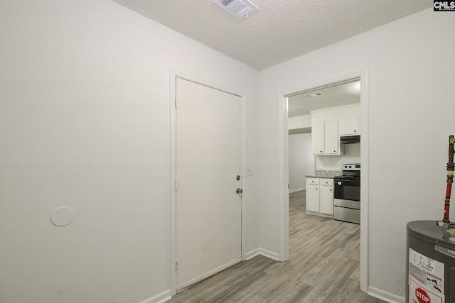 corridor with electric water heater, light wood-style floors, baseboards, and a textured ceiling