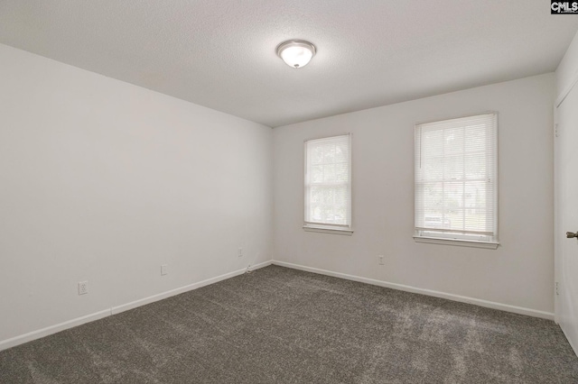 spare room with dark colored carpet, baseboards, and a textured ceiling