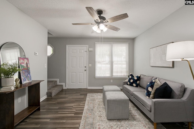 living area featuring healthy amount of natural light, a textured ceiling, ceiling fan, dark wood-type flooring, and stairway
