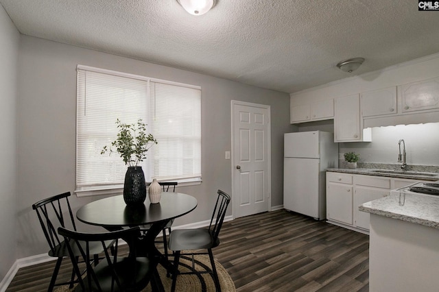 kitchen with freestanding refrigerator, a sink, a textured ceiling, white cabinets, and dark wood-style floors