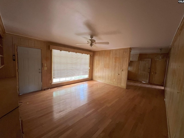 unfurnished room featuring ceiling fan, wood finished floors, wooden walls, ornamental molding, and baseboards