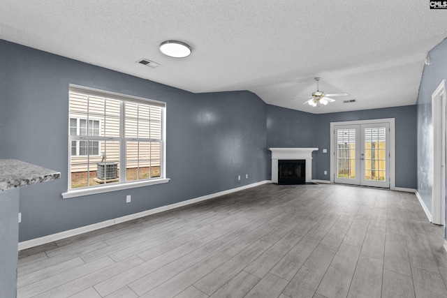 unfurnished living room with a ceiling fan, a textured ceiling, wood finished floors, baseboards, and vaulted ceiling