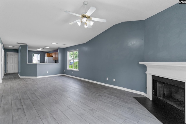 unfurnished living room with a ceiling fan, a fireplace with flush hearth, wood finished floors, lofted ceiling, and baseboards