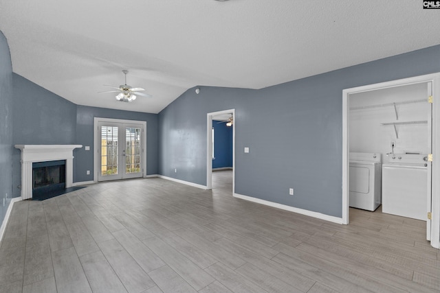 unfurnished living room featuring a ceiling fan, washing machine and clothes dryer, vaulted ceiling, a fireplace with flush hearth, and baseboards