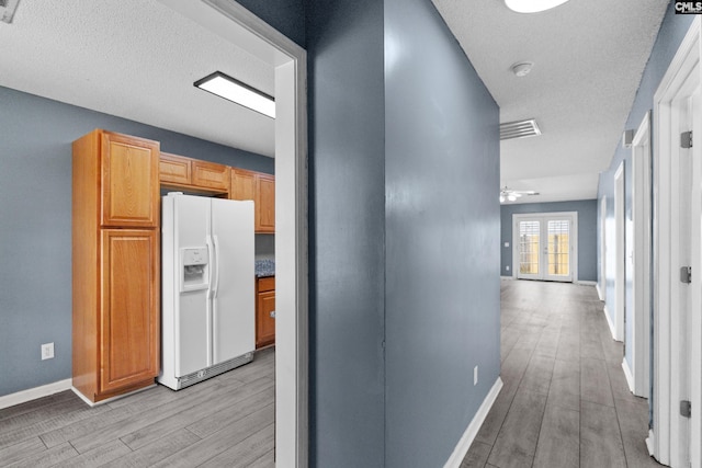 corridor featuring light wood finished floors, baseboards, and a textured ceiling