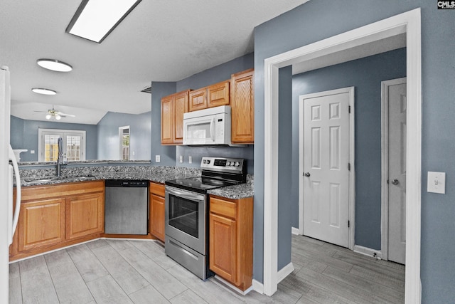 kitchen with stainless steel appliances, wood tiled floors, a ceiling fan, a sink, and dark stone countertops
