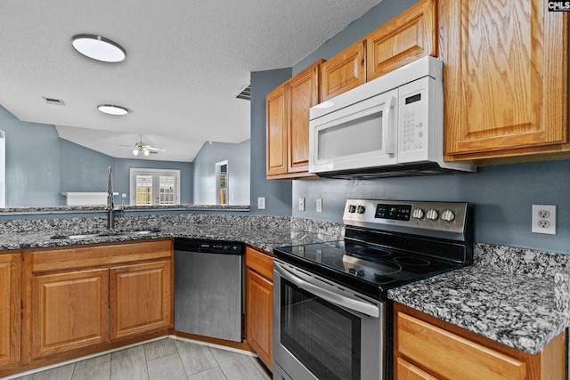 kitchen with appliances with stainless steel finishes, a sink, dark stone counters, brown cabinets, and a textured ceiling