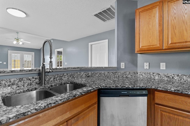 kitchen featuring dishwasher, a sink, a ceiling fan, dark stone countertops, and a textured ceiling