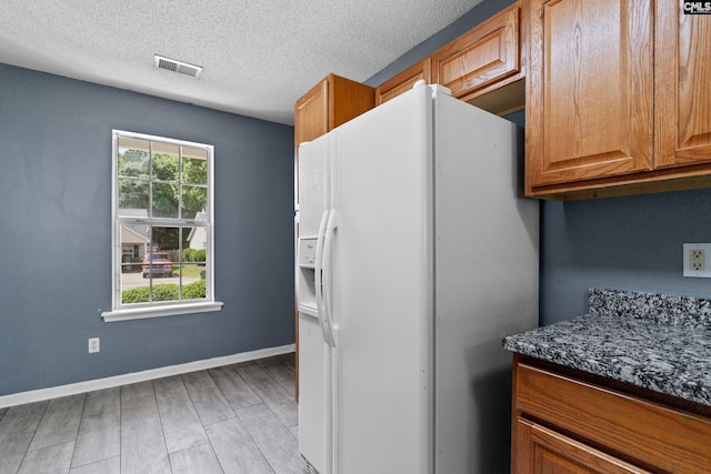 kitchen with white refrigerator with ice dispenser, light wood finished floors, brown cabinetry, a textured ceiling, and baseboards