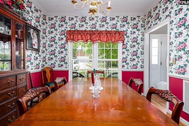 dining space with wallpapered walls, ornamental molding, a chandelier, healthy amount of natural light, and a wainscoted wall