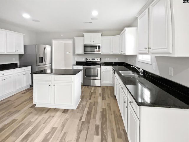 kitchen featuring appliances with stainless steel finishes, a sink, dark countertops, light wood-type flooring, and white cabinetry