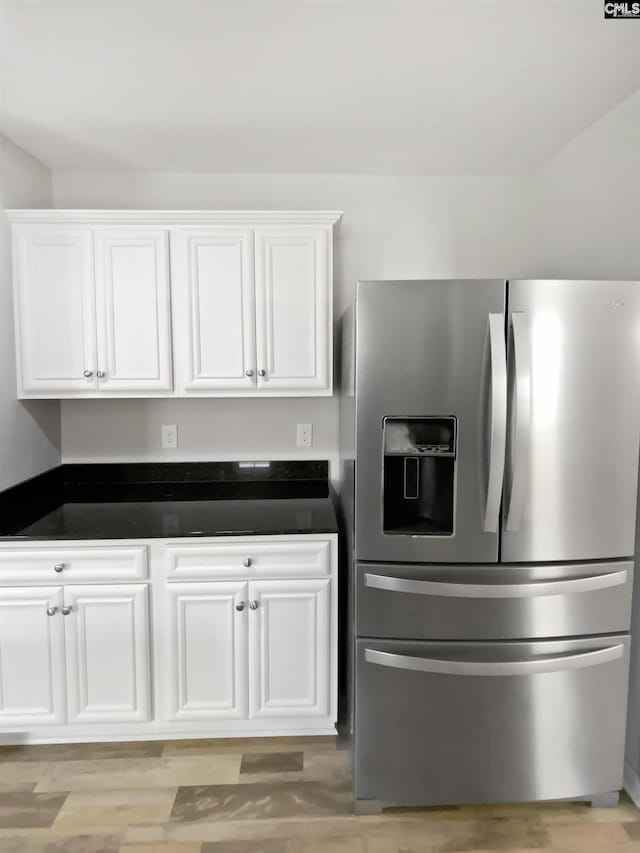 kitchen with stainless steel refrigerator with ice dispenser, dark countertops, and white cabinetry