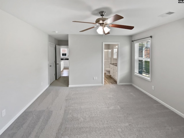 unfurnished bedroom with light colored carpet, baseboards, ensuite bath, and ceiling fan