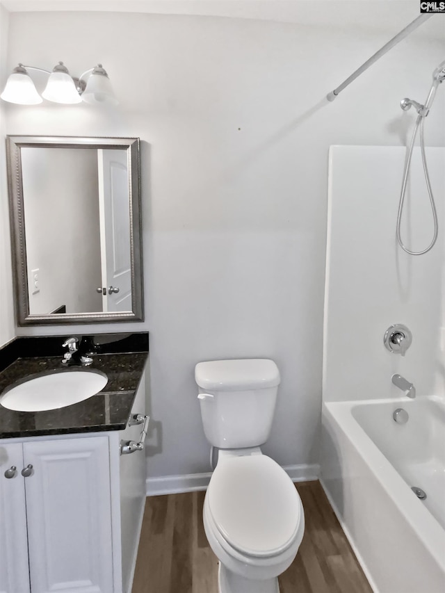 bathroom featuring wood finished floors, baseboards, toilet, vanity, and tub / shower combination