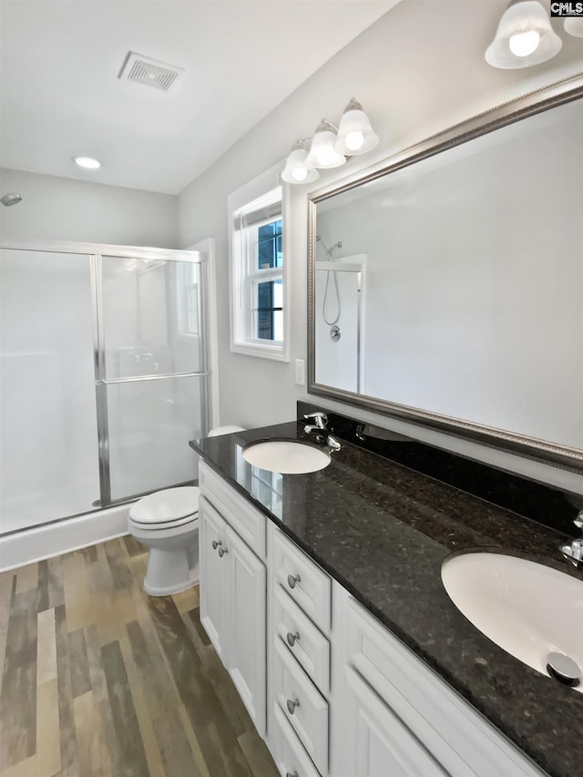 bathroom featuring a stall shower, wood finished floors, double vanity, and toilet