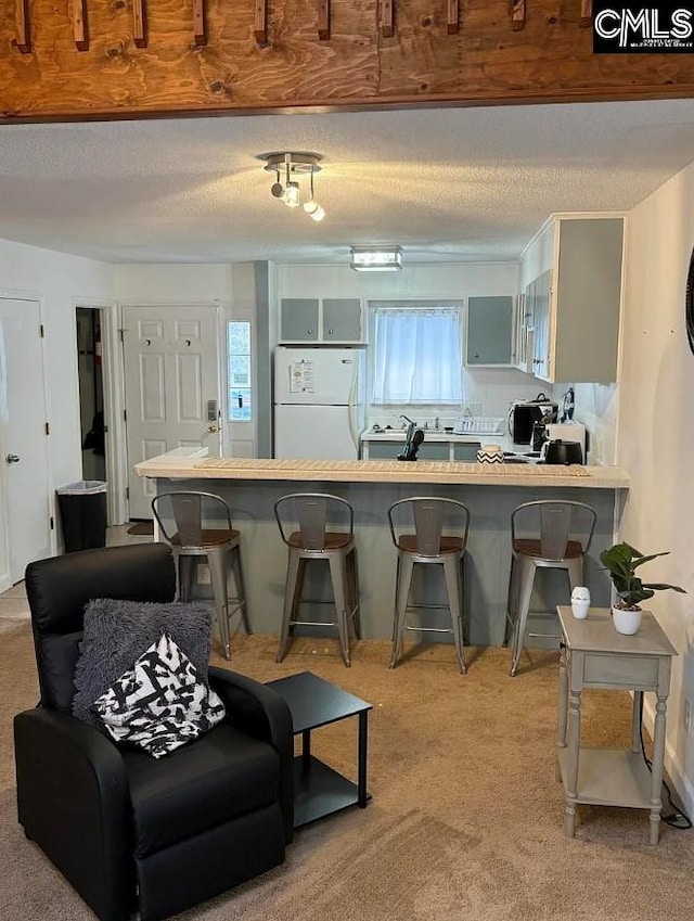 kitchen featuring freestanding refrigerator, a peninsula, a breakfast bar, light colored carpet, and a textured ceiling