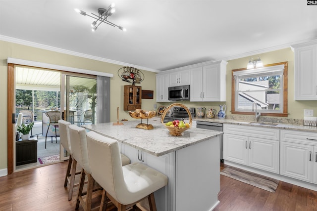 kitchen featuring stainless steel appliances, a sink, a center island, white cabinetry, and ornamental molding