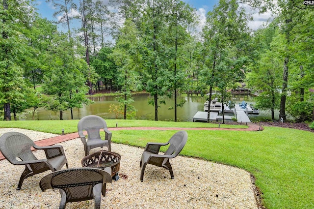 view of grassy yard with a fire pit, a water view, a dock, and view of scattered trees