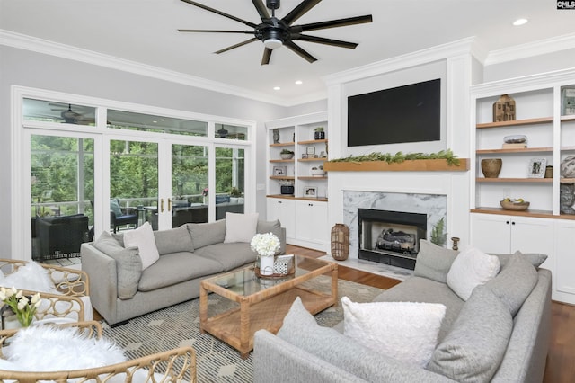 living room with a ceiling fan, ornamental molding, wood finished floors, a fireplace, and built in shelves