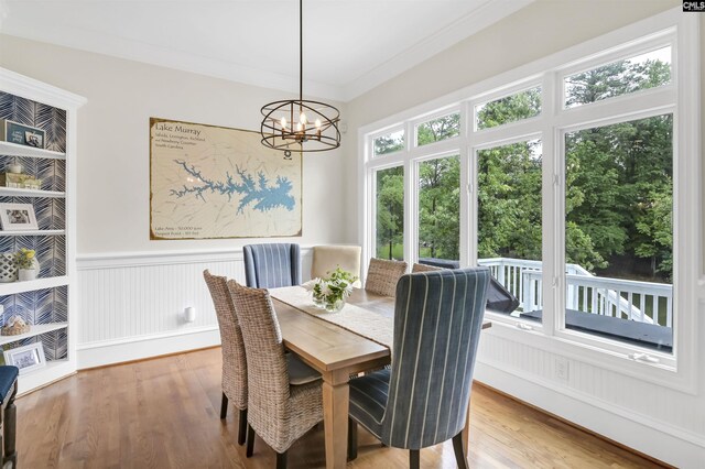 dining space with wood finished floors, wainscoting, healthy amount of natural light, a chandelier, and crown molding