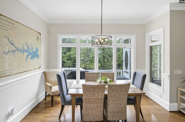 dining area featuring healthy amount of natural light, light wood-style floors, a wainscoted wall, crown molding, and a chandelier