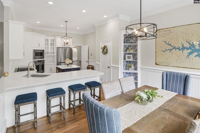 dining room with a chandelier, ornamental molding, a wainscoted wall, a decorative wall, and wood finished floors