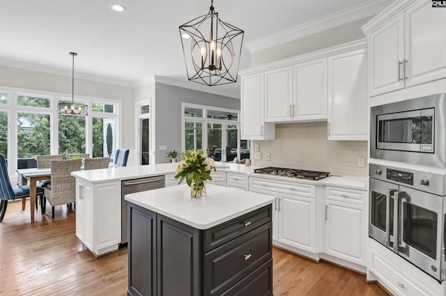 kitchen with a chandelier, appliances with stainless steel finishes, white cabinetry, light countertops, and crown molding