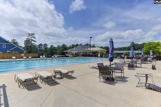 community pool with fence, a patio, and view of scattered trees