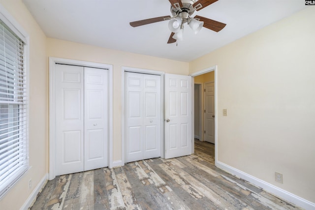 unfurnished bedroom with two closets, baseboards, and wood finished floors