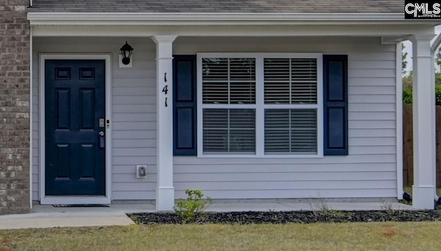 view of exterior entry featuring roof with shingles, brick siding, and covered porch