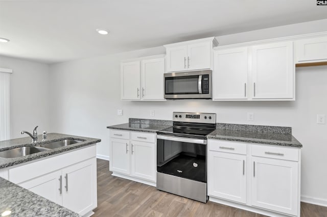 kitchen featuring appliances with stainless steel finishes, a sink, dark stone counters, white cabinetry, and wood finished floors