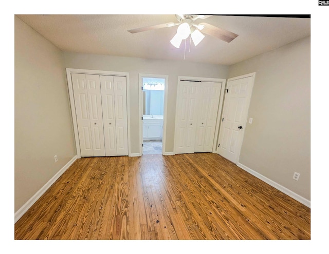 unfurnished bedroom with wood finished floors, baseboards, two closets, ensuite bathroom, and a ceiling fan