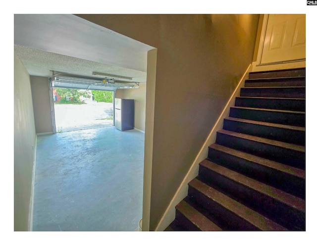 stairs featuring concrete flooring, baseboards, and a textured ceiling