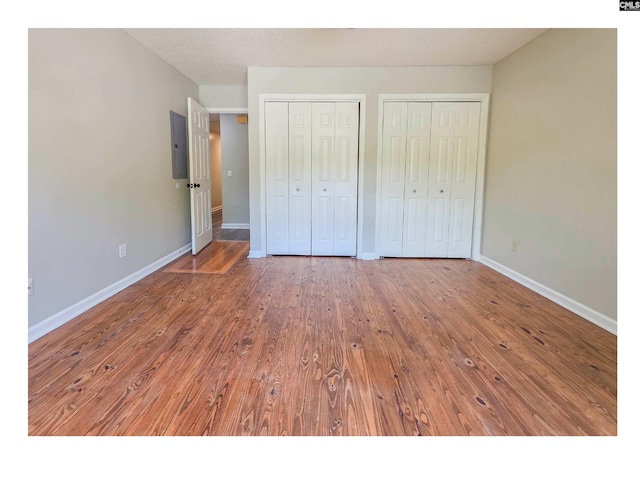unfurnished bedroom featuring two closets, baseboards, and hardwood / wood-style floors