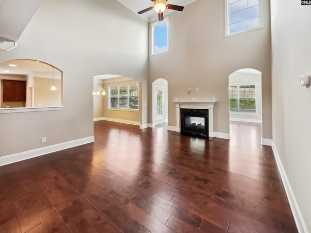 unfurnished living room with a ceiling fan, a towering ceiling, dark wood-style floors, a multi sided fireplace, and baseboards