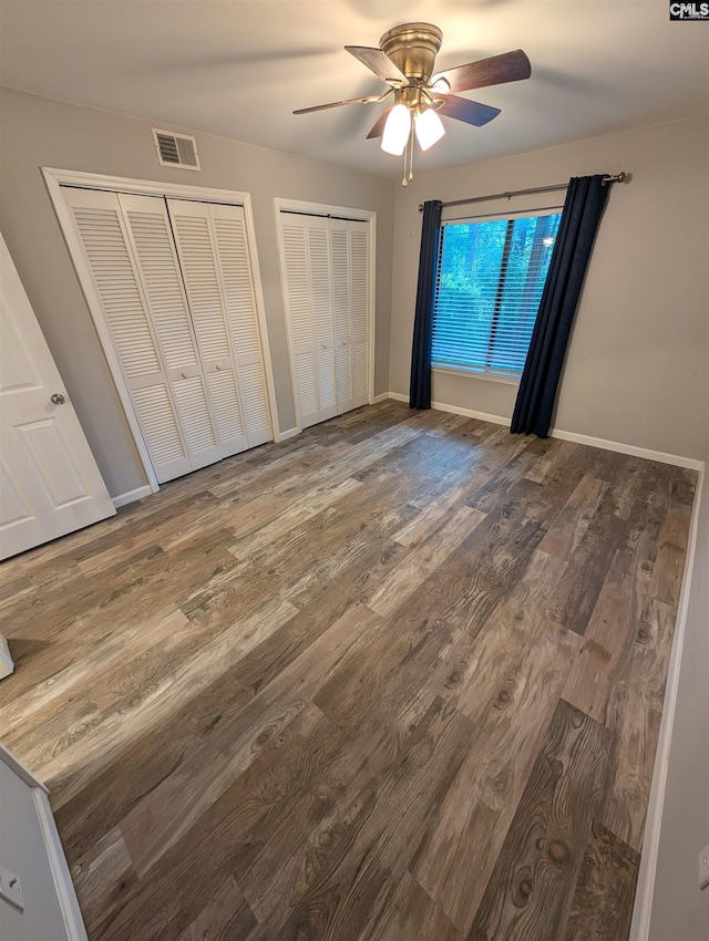 unfurnished bedroom with multiple closets, wood finished floors, a ceiling fan, and baseboards
