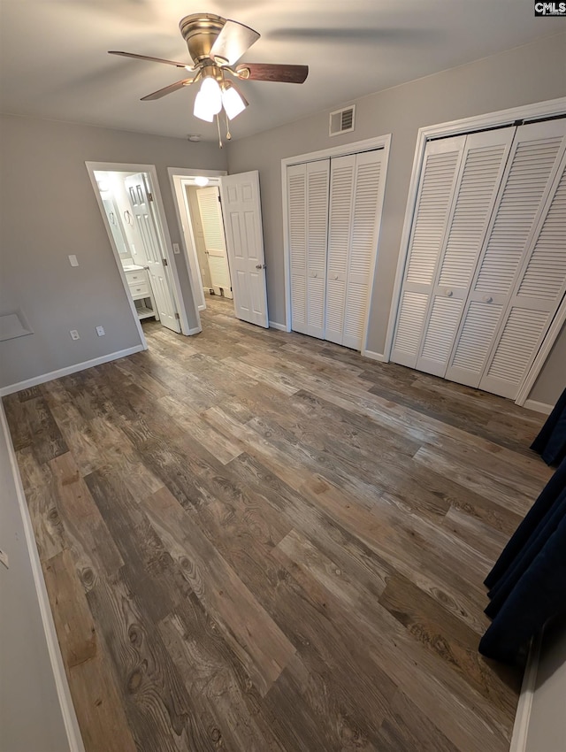 unfurnished bedroom with wood finished floors, two closets, baseboards, ceiling fan, and ensuite bathroom