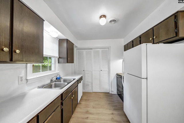 kitchen with freestanding refrigerator, a sink, dishwasher, dark brown cabinets, and light wood-style floors