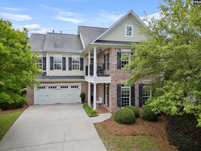 view of front of property featuring a balcony, a garage, driveway, brick siding, and a shingled roof