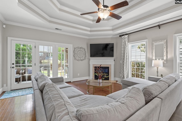 living room with a tray ceiling, ceiling fan, a glass covered fireplace, hardwood / wood-style flooring, and crown molding