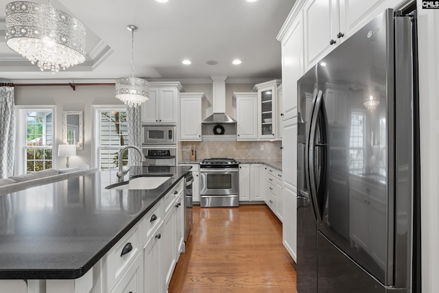 kitchen featuring appliances with stainless steel finishes, wall chimney range hood, a sink, white cabinets, and crown molding