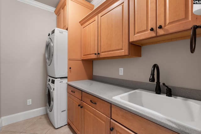 clothes washing area with stacked washing machine and dryer, cabinet space, light tile patterned floors, baseboards, and ornamental molding