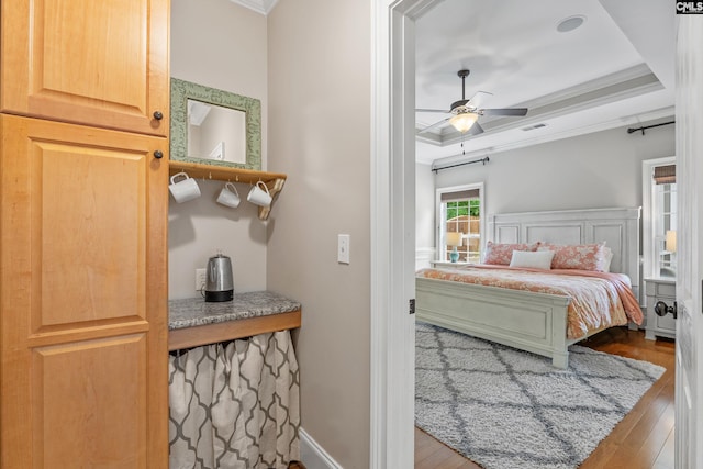 bedroom with wood finished floors, ornamental molding, a raised ceiling, and ceiling fan