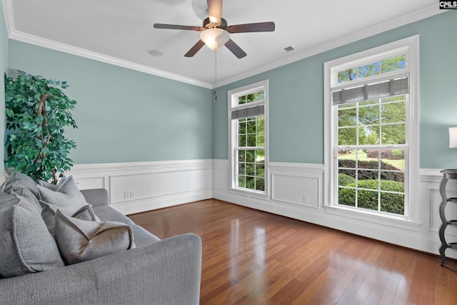 living area with plenty of natural light, wainscoting, crown molding, hardwood / wood-style flooring, and ceiling fan