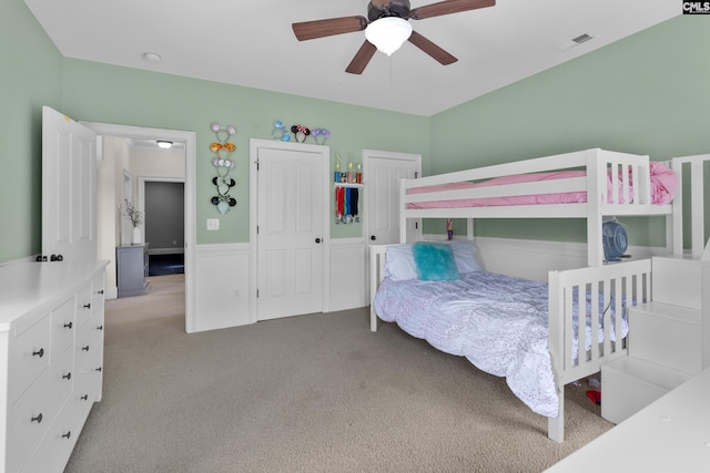 bedroom featuring carpet, a ceiling fan, and a wainscoted wall